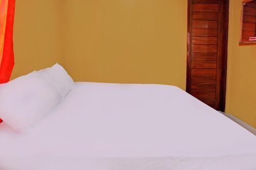 a bedroom with a white bed and a yellow wall at Hotel O Ujung Samalas HomestayNearLapangan Sembalun Bumbung in Labuan Lombok