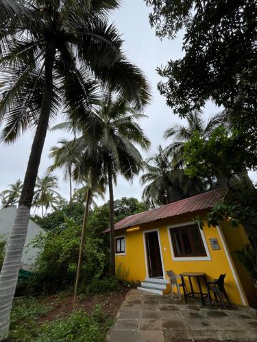 a yellow house with two chairs and palm trees at GOAROUND- Portuguese Villa at Anjuna Beach by Goaround Homes in Anjuna