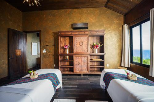 a bedroom with two beds and a cabinet and windows at Prana Maya Island Resort in Placencia Village