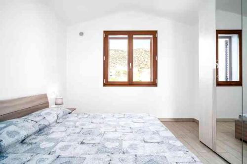 a white bedroom with a bed and a window at CASE ORCHIDEA - ROSA BLU in La Caletta