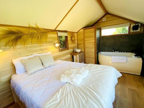 - une chambre avec un grand lit blanc et une baignoire dans l'établissement La cabane balnéo vue mer, à Bazenville