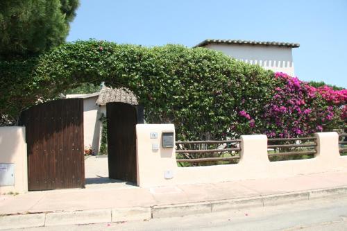 a fence with a wooden gate and a hedge with pink flowers at Casa Stella Di Madel in Flumini di Quartu