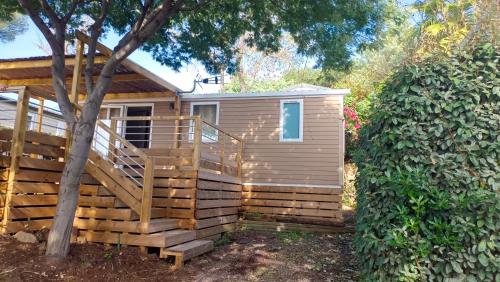 a small house with a wooden deck next to a tree at Mobilhome neuf à Camping Domaine l'Ile d'Or à Saint Raphaël in Saint-Raphaël