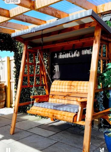 a wooden swing with a roof on a patio at Barlosh Barony Tpod Lodge Ayrshire, elec jacuzzi, BBQ, Firepit, Pizza Oven, indoor outdoor terrace with amazing views, spacious inside and out in Ochiltree