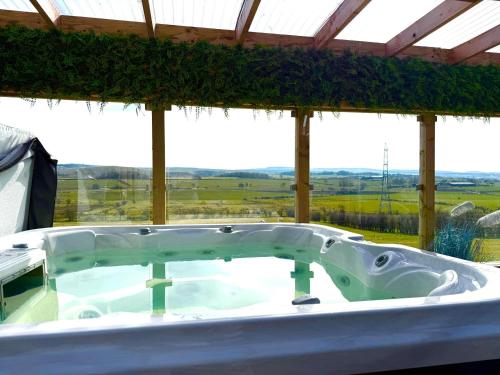 a bath tub with a view of a field at Barlosh Barony Tpod Lodge Ayrshire, elec jacuzzi, BBQ, Firepit, Pizza Oven, indoor outdoor terrace with amazing views, spacious inside and out in Ochiltree