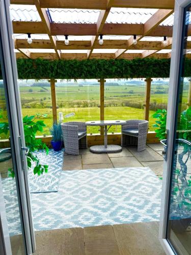 a patio with a table and chairs under a pergola at Barlosh Barony Tpod Lodge Ayrshire, elec jacuzzi, BBQ, Firepit, Pizza Oven, indoor outdoor terrace with amazing views, spacious inside and out in Ochiltree