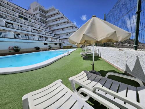 a pool with two white chairs and an umbrella at Vista Calma Suite Puerto Rico in Puerto Rico de Gran Canaria