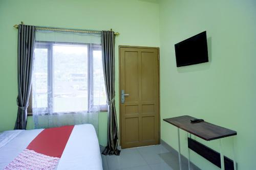 a bedroom with a bed and a desk and a window at Hotel O Parapat Near Dermaga Ajibata Formerly Pudan Residence 2 in Parapat