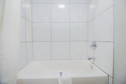 a white bathroom with a tub and a white tile wall at OYO Hotel McAlester OK S Main St in McAlester