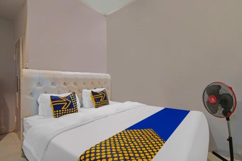 a bed with yellow and blue pillows and a fan at Hotel O Putri Guest House Syariah Near SPBU Rimbo Panjang in Pekanbaru