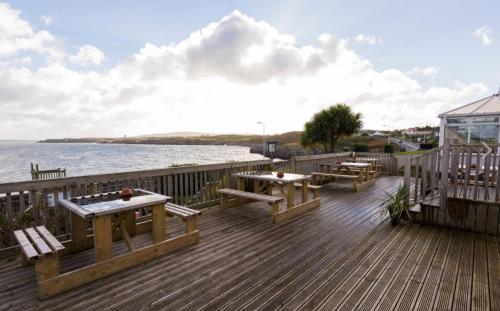 a wooden deck with picnic tables and the water at Trecastell Hotel in Amlwch