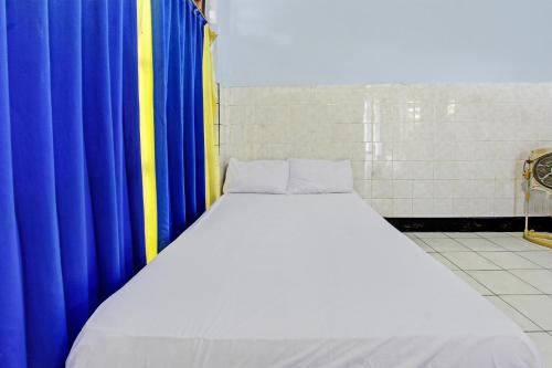 a large bed in a room with blue and yellow curtains at Hotel O Mareje Sariguna in Mataram