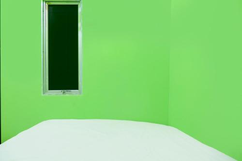 - un lit blanc dans une chambre verte dotée d'une fenêtre dans l'établissement Hotel O Joyoakis 2 Homestay SyariahNearMall Nagoya Hill, à Nagoya