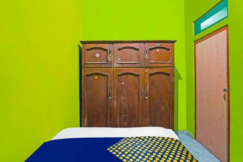 a green room with a bed and a wooden door at Hotel O Homestay Barokah in Gresik