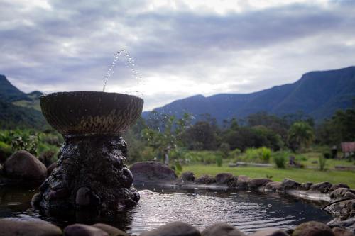 a fountain in a pond with mountains in the background at Figueira do Rio do Boi Com Hidromassagem in Praia Grande