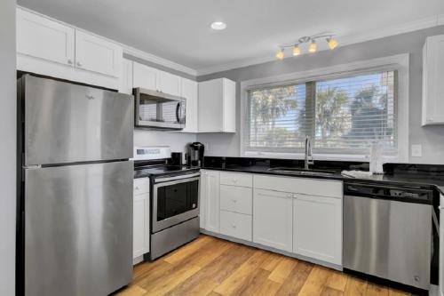 a kitchen with white cabinets and a stainless steel refrigerator at Seagrove 1A by Wild Dunes, Oceanfront Condo in Isle of Palms