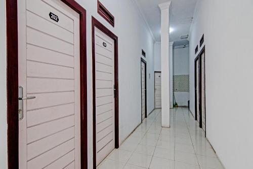 a corridor with white doors and white tile floors at Hotel O Lestari Baru Syariah Near SMA Negeri 1 Salo in Bangkinang