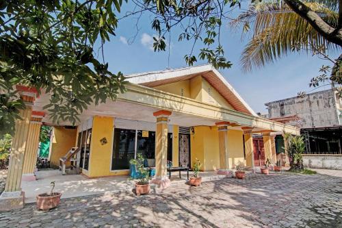 a yellow house with potted plants in a courtyard at Hotel O Meranti HomestayNearJembatan Siak in Pekanbaru