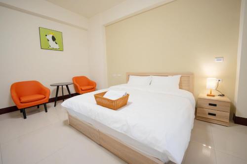 a white bedroom with a bed and two orange chairs at 夏米旅宿 in Lugang