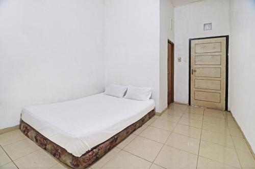 a white bedroom with a bed and a door at Hotel O Arizona Homestay in Jambi