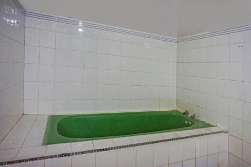 a green bath tub in a white tiled room at Hotel O Triarga in Takengon