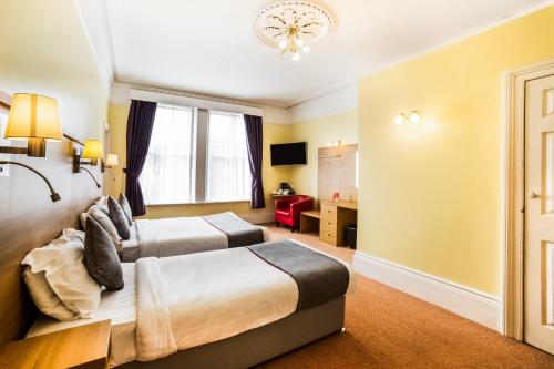 two beds in a hotel room with yellow walls at OYO Eagle House Hotel, St Leonards Hastings in St. Leonards