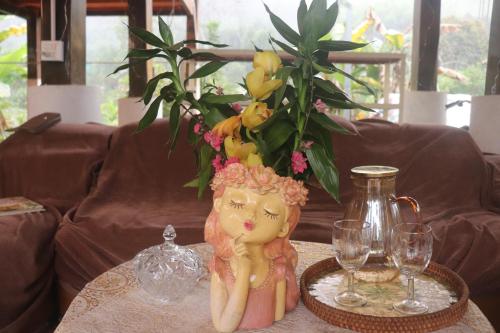 a doll sitting on a table with glasses and a vase at Atash Eco Village Homestay Van Hoi in Quân Khê