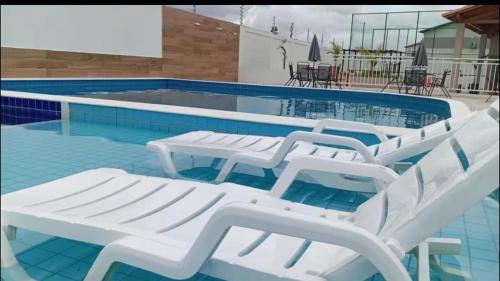 a group of white lounge chairs in a swimming pool at Casa em Parnaíba lazer e praia in Parnaíba