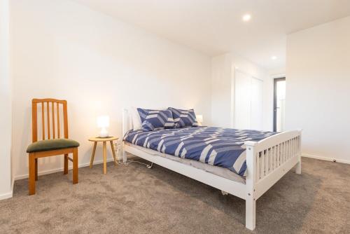 a white bedroom with a bed and a chair at Brand new 2 bed ocean view! in Christchurch