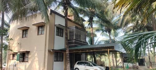 a white car parked in front of a building with palm trees at KV Farm house in Malaiyāndipattanam