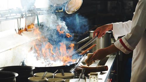 a chef cooking food on a grill in a kitchen at Golden Tulip Mandison Suites in Bangkok