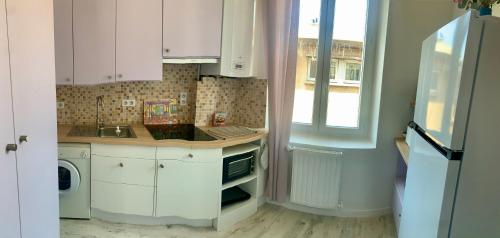 une cuisine avec des armoires blanches, un évier et une fenêtre dans l'établissement Appartement cosy lumineux et calme, à Apt