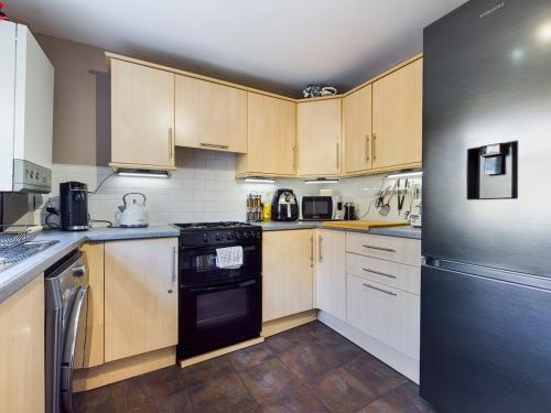 a kitchen with wooden cabinets and a black refrigerator at Duck Cottage beautiful views countryside village in Delph