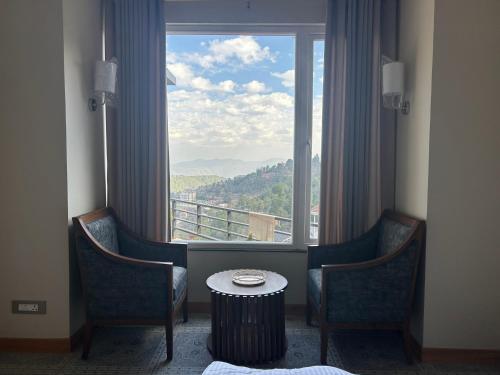 a room with two chairs and a table in front of a window at VAAS Cottage in Mukteshwar