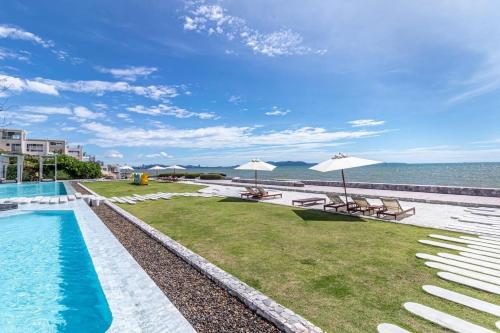 a pool with chairs and umbrellas next to the ocean at Veranda Pattaya Sea View Jomtien Beach Front วิวทะเล พัทยา จอมเทียน in Na Jomtien