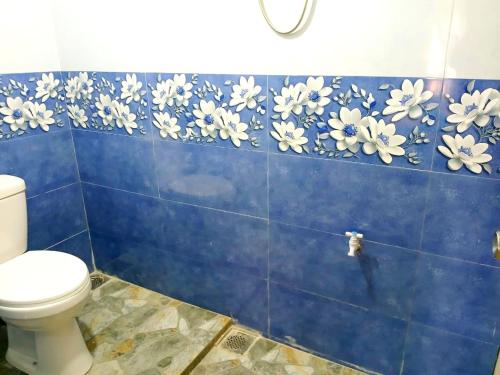 a blue tiled bathroom with a toilet and flowers on the wall at Dio Green House NUWRA ELIYA in Nuwara Eliya