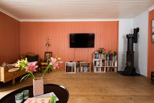 a living room with an orange wall with a flat screen tv at Experience Jotunheimen from Vevstogo - sauna with a view and eco living in an old school building in Løken