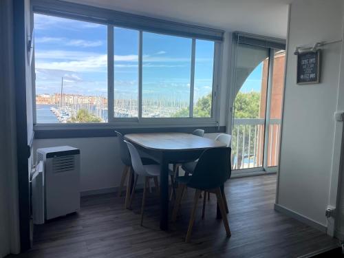 une table et des chaises dans une pièce avec une grande fenêtre dans l'établissement Gruissan Appartement Cosy Vue Port, à Gruissan