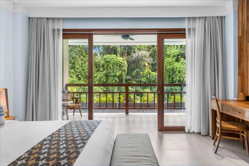 a bedroom with a bed and a desk and a large window at Vije Boutique Resort & Spa in Ubud