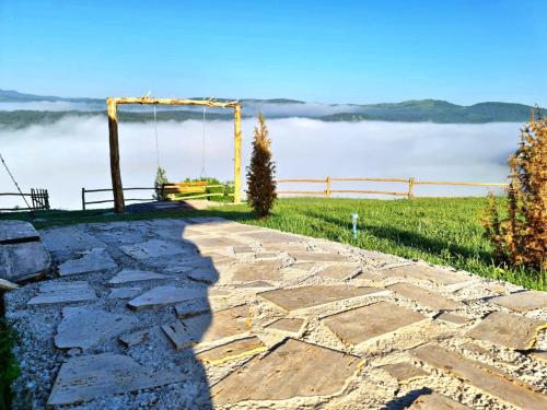 a stone walkway with a swing and a view of a foggy field at Ethno village Molitva in Družiniće