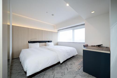 a bedroom with a large white bed and a desk at Hotel Sunroute Tokushima in Tokushima