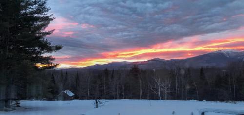 a sunset in the mountains with snow and a tree at Holden Frost House in Franconia