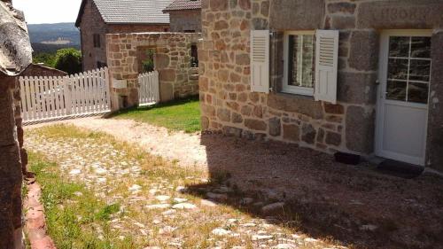 a brick building with a white fence and a window at Gîte La Maison d'Alphonse 7/8 personnes in Saint-Léger-du-Malzieu