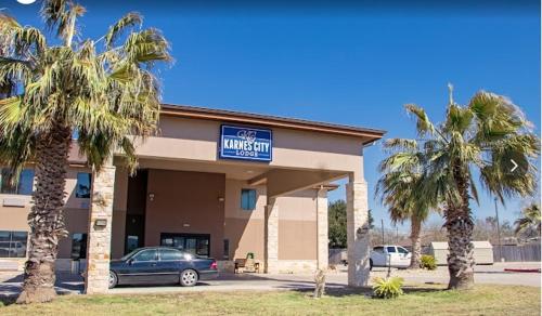 a hotel with palm trees in front of a building at Karnes City Lodge in Karnes City