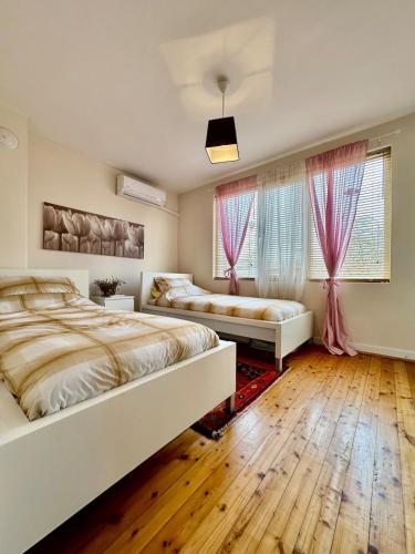 two beds in a bedroom with wooden floors and pink curtains at Mary's Guesthouse in Banya