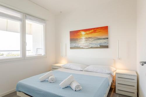 a white bedroom with two beds and a painting on the wall at La Terrazza sul Mare with parking in Lignano Sabbiadoro