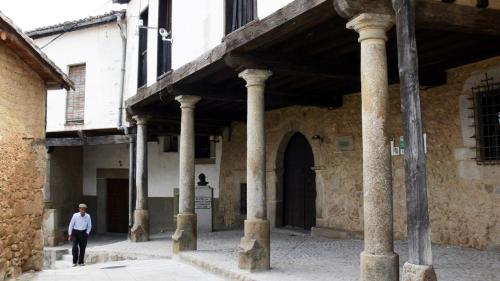 a man walking down a street next to a building with columns at Hotel Moregón in Cuacos de Yuste
