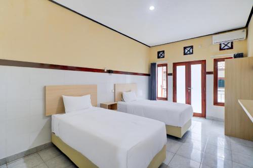 a hotel room with two beds and two windows at Townhouse Oak Legian Near Legian Beach Formerly Sayang Maha Merta in Legian