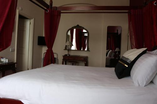 a bedroom with a large white bed with red curtains at The Belgrave Hotel Tenby in Tenby