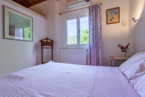 a bedroom with a white bed and a window at Charming Pink Villa in Skopelos Town